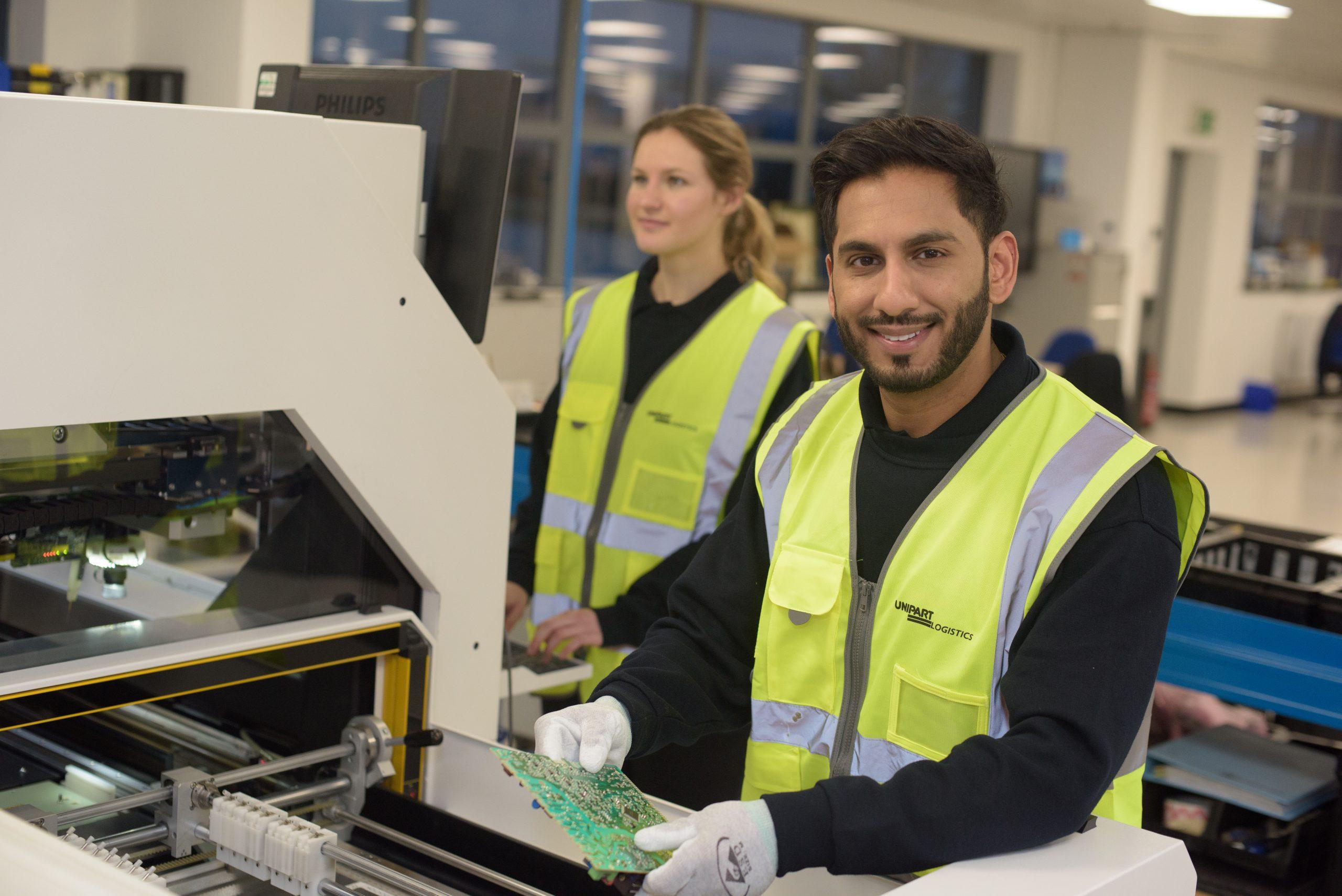 Unipart colleagues working at a work station and smiling.